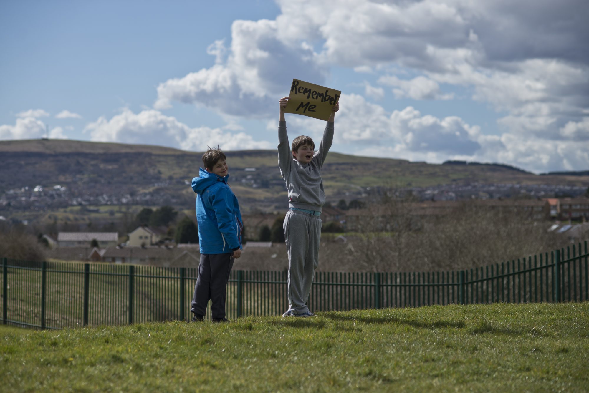 Two people stand on a hill, one holds a sign above his head