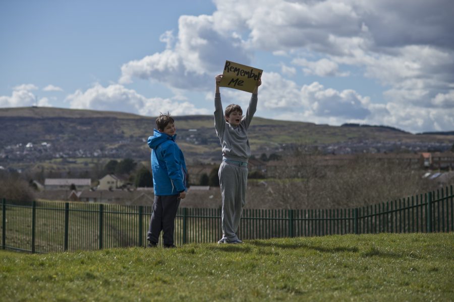 Two people stand on a hill, one holds a sign above his head