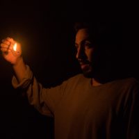 A photo of a cast member holding up a match in a dark space