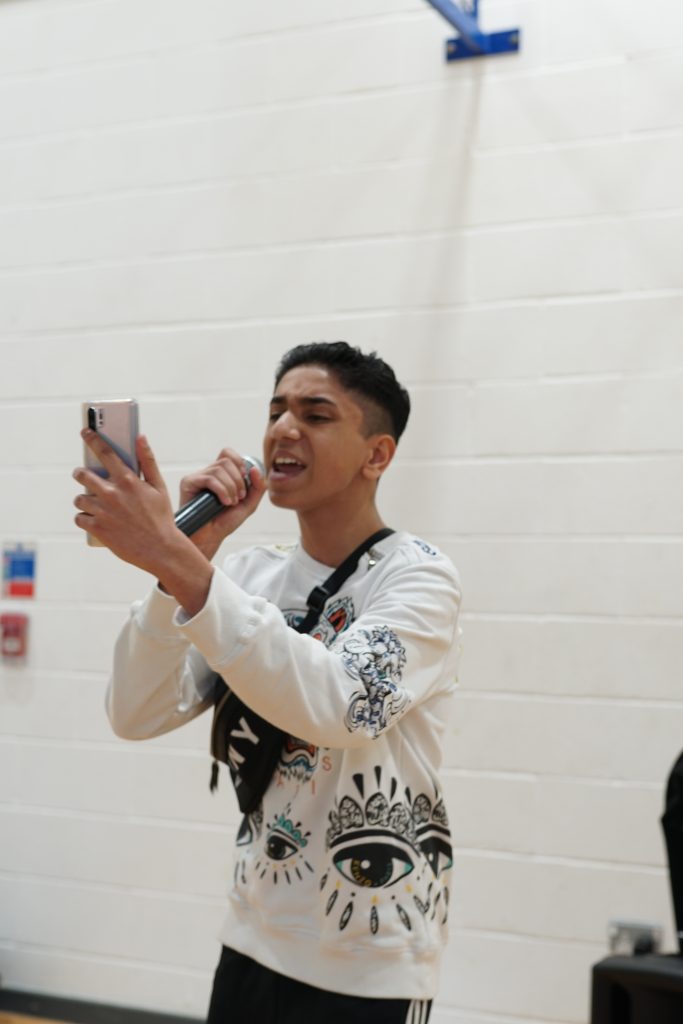 A teenage boy performs into a mic whilst looking at his phone