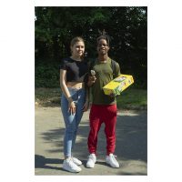 A young white woman and a young black man stand together in the sunshine. He is holding a box of Cocoa Pops