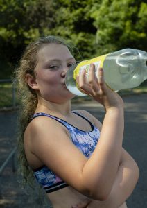 A teenage girl drinks from a lemonade bottle whilst looking at the camera.