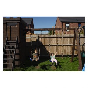 Two kids swing on swings in a garden