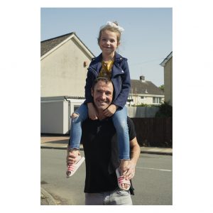 A man has his daughter sitting on his shoulders in the street