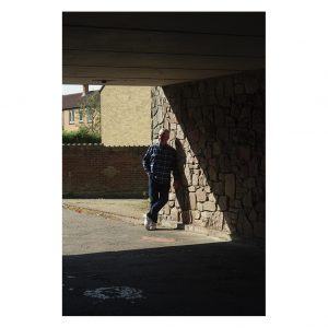 A man leans in the wall in an underpass. He is standing in the sunshine.