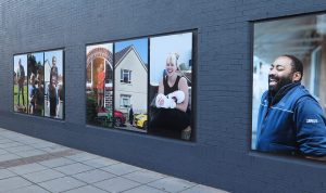 an installation of larger than life photographic portraits outdoors, on a grey wall.