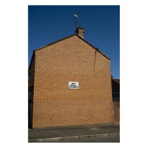 The side of a house against a blue sky. There is a sign saying 'no ball games'