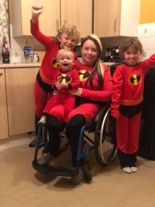 Rhian a'i thri phlentyn wedi gwisgo fel 'The Incredibles'. Mae Rhian yn eistedd mewn cadair olwyn, yn dal ei phlentyn ieuengaf ar ei glin.