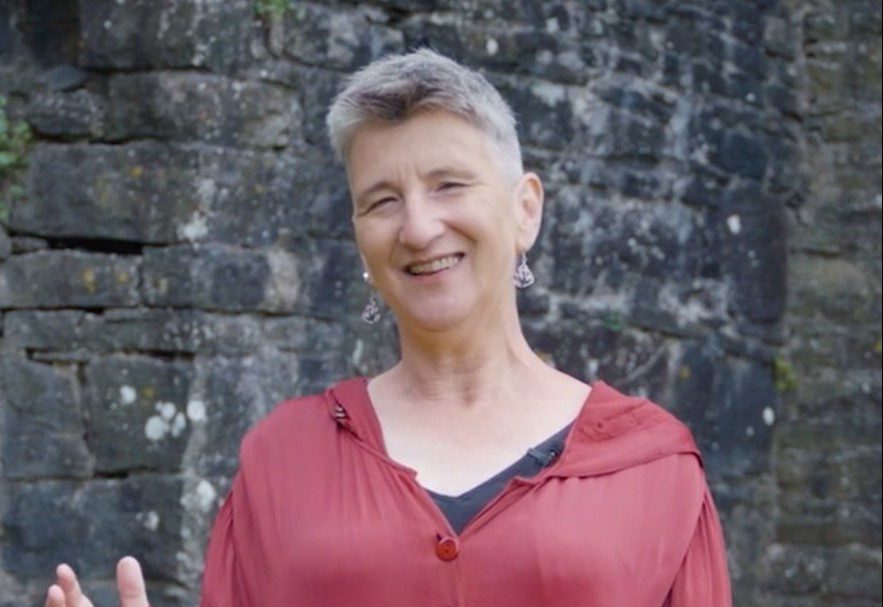 A woman in a red top looks at the camera.