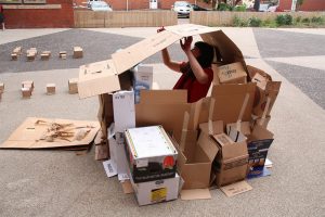 A woman sits in a cardboard house