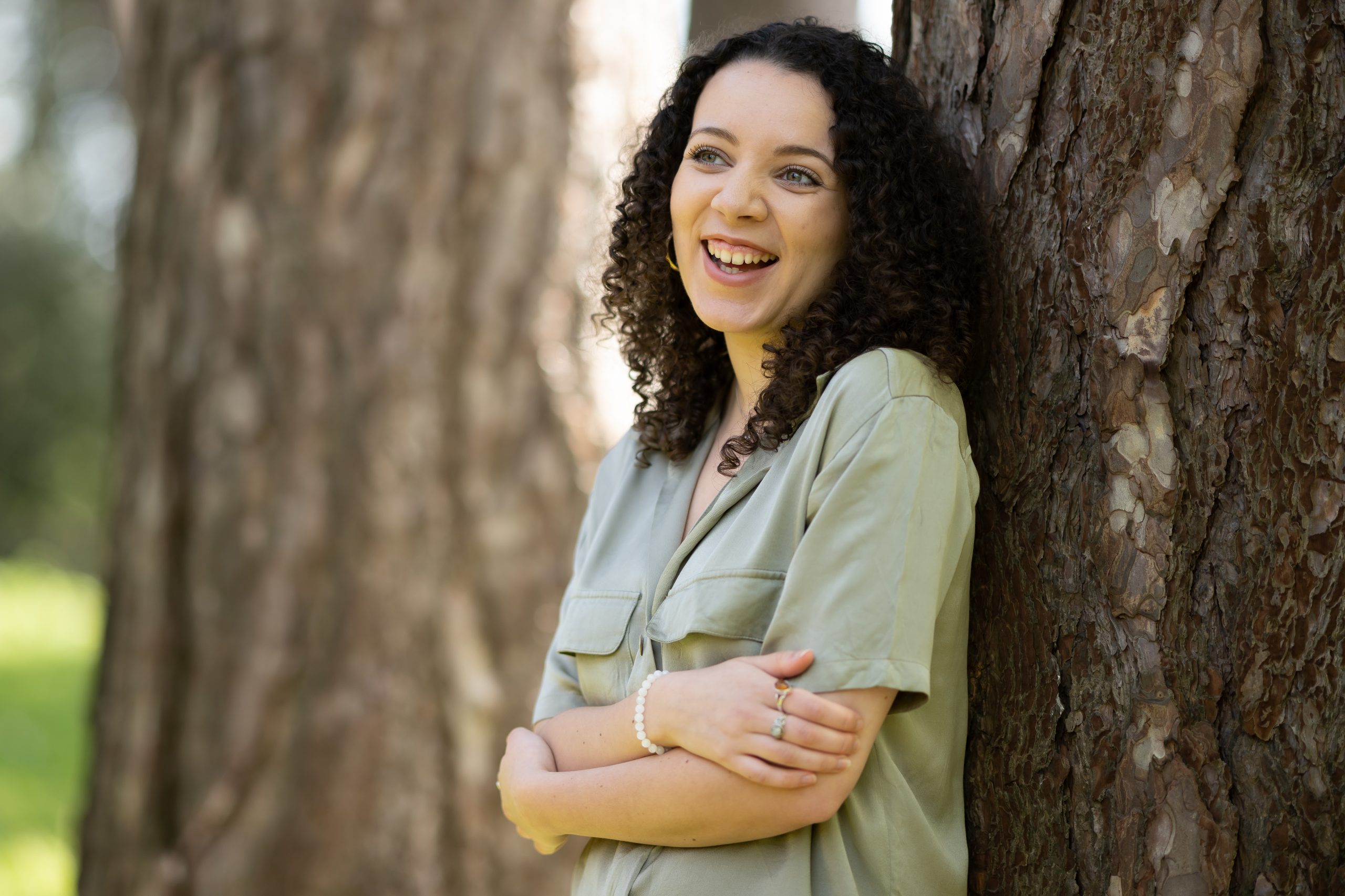 A woman, wearing a light green shirt, leans against a tree.