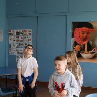 Two boys and a girl stand in a classroom with blue walls.