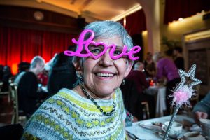 An older lady wears pink glasses in the shape of the word "love"