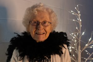 An older lady smiles. She's wearing a black feather boa.