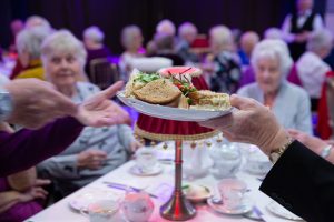 a plate of triangle cut sandwiches are being passed between two hands