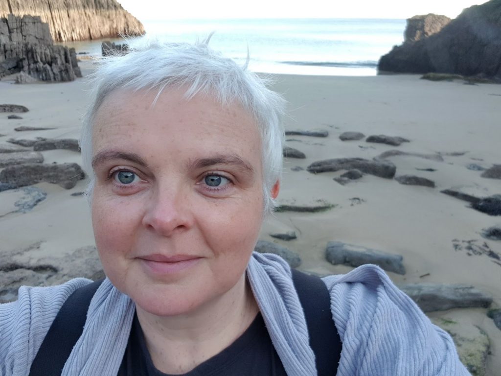 A white woman with short white hair, on a beach.