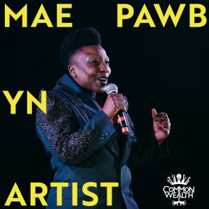 The words "MAE PAWB YN ARTIST" are laid on top of an image of a black person with short hair, wearing a blue sparkly suit, singing into a microphone
