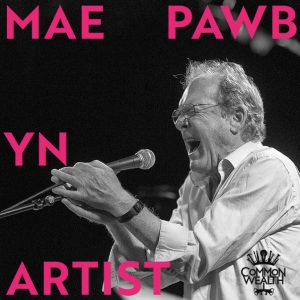 The words "Mae Pawb yn artist" in blue are laid on top of a black and white image of a white man singing really loudly into a microphone