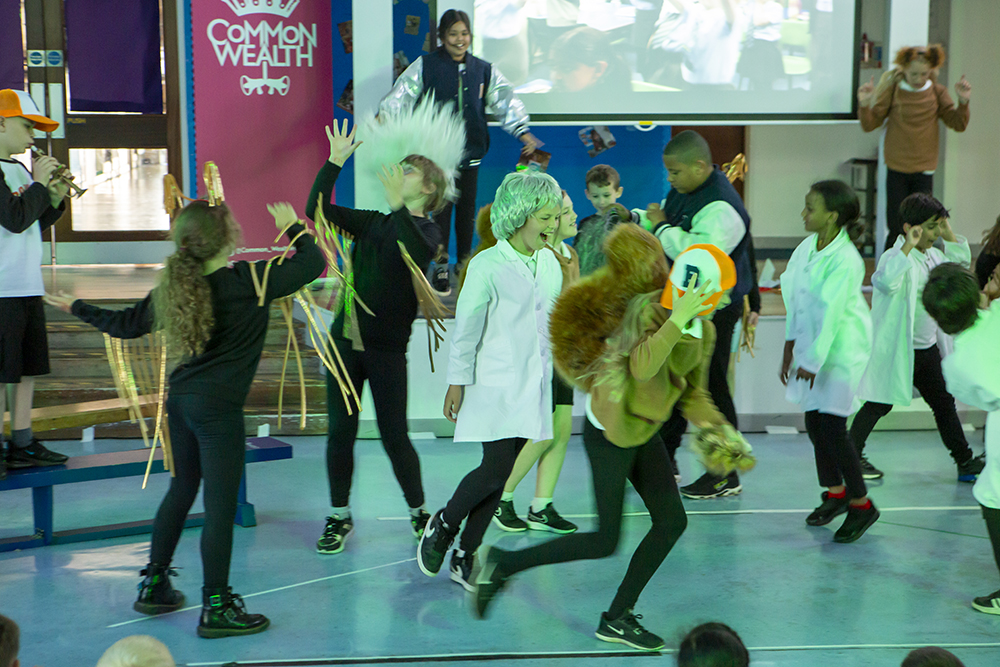 Kids dressed as squirrels and scientists run around a school hall as part of a perfromance