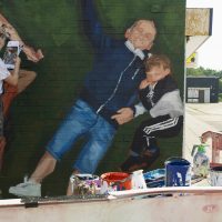A close up of the mural showing the artist at work, beside a painted man with his small child