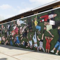 A wide shot of large, colourful mural showing over 50 people lying on the grass