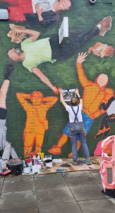 Helen Bur paints the mural - this photo shows unfinished people in orange