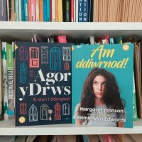 Two Welsh language books, aimed at learners, on a bookshelf.