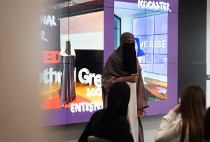 Facilitator wearing a niqab talks to young people, demonstrating something on a digital screen for them.