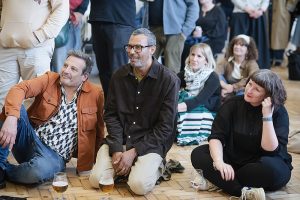 Audience members sitting on the floor and listening to poetry.