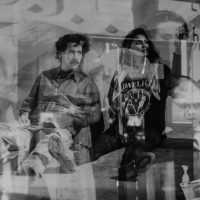Performers Soul Roberts and Hussina Raja sit on the floor, with images from the projections layered over their bodies 