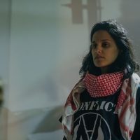 Hussina Raja, wearing a keffiyeh and a political t-shirt, gazes at the floor 