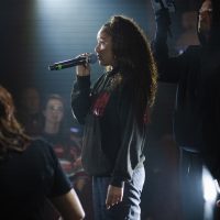 Performer Bianca Ali is spotlit by white light as she sings in a microphone