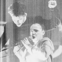 A distorted image of a woman shouting into a microphone with a man dancing behind her