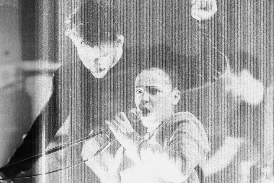 A distorted image of a woman shouting into a microphone with a man dancing behind her
