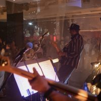 Band Kamikaze Rainbow perform for the audience. The photograph shows a close up of two band members playing on their guitars with the audience behind them